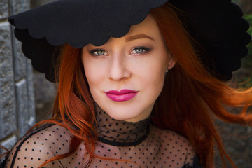 portrait of stylish young beautiful red-haired girl in a black hat near the stone wall - 203177011