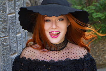 portrait of stylish young beautiful smiling red-haired girl in a black hat near the stone wall - 203177220
