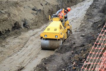 road roller compacts the sand in a deep trench.