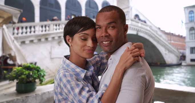 Romantic African-American couple in Venice, Italy embracing each other closely, Attractive young black male and female posing together intimately near the Rialto Bridge, 4k