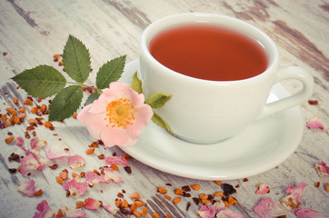 Vintage photo, Cup of tea with wild rose flower on old rustic board