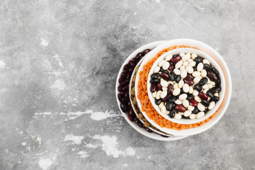 Assortment of beans (red lentil, green lentil, chickpea, peas, red beans, white beans, mix beans, mung bean) on gray background. Top view, copy space. Food background