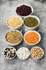 Obraz na płótnie Canvas Assortment of beans (red lentil, green lentil, chickpea, peas, red beans, white beans, mix beans, mung bean) on gray background