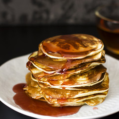 Homemade pancake poured syrup drops in white plate on dark background, closeup