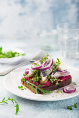 smorrebrod, open sanwich with dark rye bread, beet, marinated herring, pickled cucumber and red onion
