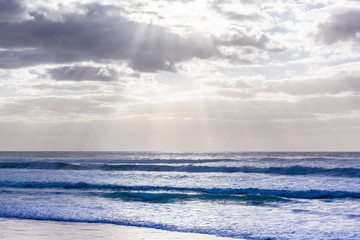 Beautiful seascape with sun rays through clouds and ocean waves