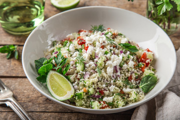 couscous and vegetables salad with feta cheese in white bowl