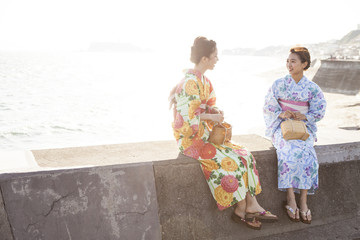浴衣を着た女性たちは堤防に座っておしゃべりしている