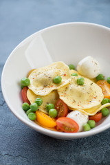 White bowl with ravioli, mozzarella, cherry tomatoes and green peas, selective focus, vertical shot