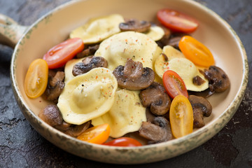 Close-up of a serving pan with italian ravioli, fried champignon slices and cherry tomatoes, studio shot