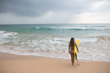 Woman surfer looking at the ocean with a surfboard in his hands.