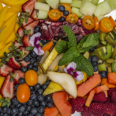 A plate of colorful, delicious, locally sourced fruit includes berries, melon, mango, kiwi, kumquats and a mint garnish.