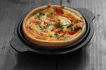 Tomato and spring onion quiche in a cast iron pot dish on a wood background with selective color