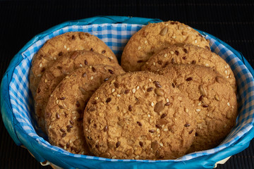 homemade oat cookies with sunflower seeds in and near blue checkered basket on black background