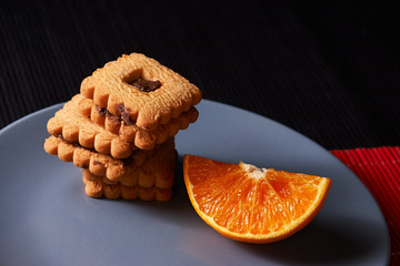 Chocolate chip cookies and piece of orange on plate and on red and black background with place for text selective focus with copyspace