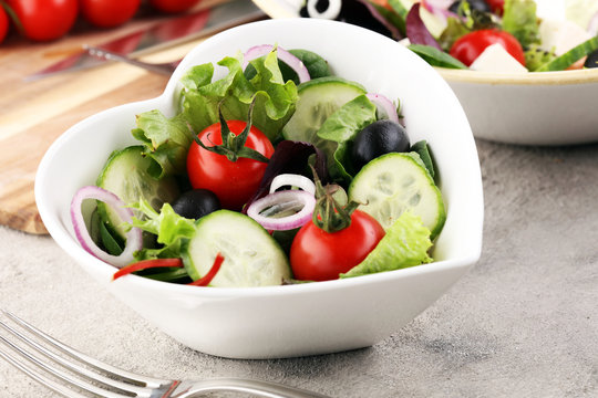 bowl of salad with vegetables and greens, with tomato, cucumber and onions.