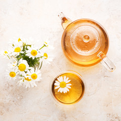 Chamomile herbal tea in a teapot and cup on a beige stone background, top view