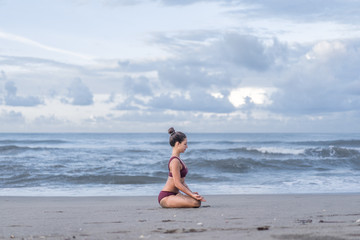 side view of fit young woman meditating in lotus pose (padmasana) with gyan mudra on seashore