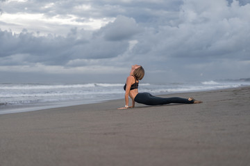 Fototapeta na wymiar side view of sportive young woman practicing yoga in Upward-Facing Dog pose (Urdhva Mukha Svanasana) on seashore
