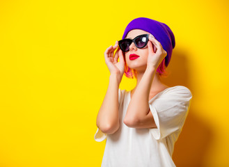Young girl with pink hair in purple hat and sunglasses on yellow background