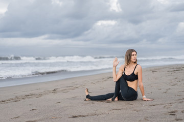 fit young woman practicing yoga in Marichis III pose on seashore