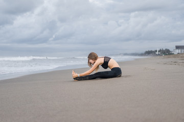 Fototapeta na wymiar attractive young woman practicing yoga in Caterpillar pose on seashore