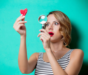 Young woman with magnifying glass and heart on green background