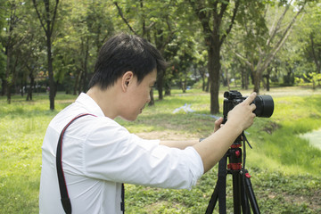 Asian man photographing in the park.  Professional travelling photographer and artist.  Profile view.