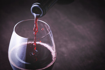 Pouring red wine into the glass against wooden background