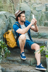 handsome young man taking photo with smartphone while sitting on stone staircase