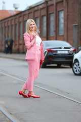Woman in pink suit and with umbrella crossing the road