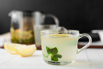 Ginger tea with mint, lemon and honey in a glass cup on a white wooden table