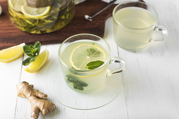 Ginger tea with mint, lemon and honey in a glass cup on a white wooden table
