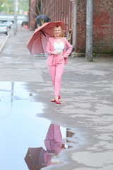 Woman in pink suit with umbrella walking on the street after the rain