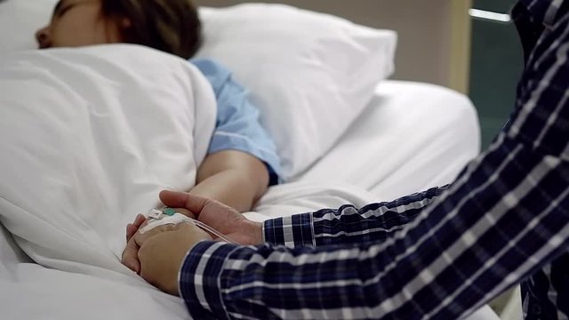 Man hand encourages his wife sleeping on bed in hospital, Male hand holding and consoling woman patient hand in hospital. Encouragement from family, healthy and comfort concept.