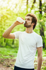 Young man is exercising in park. He is drinking water. 