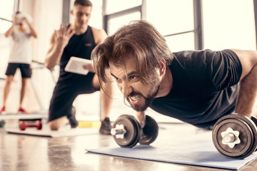 Fototapeta na wymiar angry sportsman doing push ups on dumbbells in gym