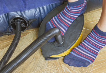 A woman with air foot pump pumps an inflatable mattress or air bed at home. Part of body, selective...