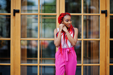 Fashionable african american girl at pink pants and red dreads posed outdoor.