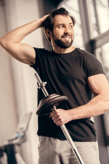 smiling sportsman holding iron bar and touching hair in gym