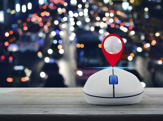 Map pin location button with wireless computer mouse on wooden table over blurred colourful night...