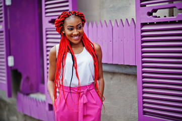 Fashionable african american girl at pink pants and red dreads posed outdoor.