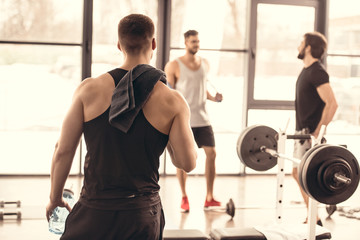 Fototapeta premium back view of muscular sportsman looking at friends in gym