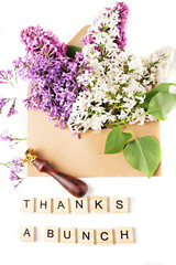 Close up of opened craft paper envelope filled with spring blossom purple and white lilac flowers laying on white background. Top view. Concept of gratitude.