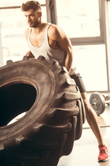 Obraz na płótnie Canvas athletic young man in sportswear training with tire in gym