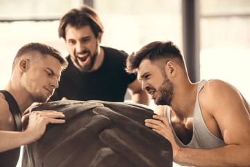 man looking at concentrated sportsmen lifting tire in gym