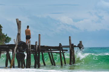  Man standing at the pier and watching the ocean waves. Lazy beach, Koh Rong Samloem. Cambodia.