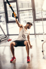 athletic young man in sportswear exercising with suspension straps in gym