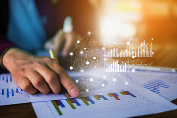 Close up Businessman hand holding pen and pointing at financial paperwork with financial network diagram.
