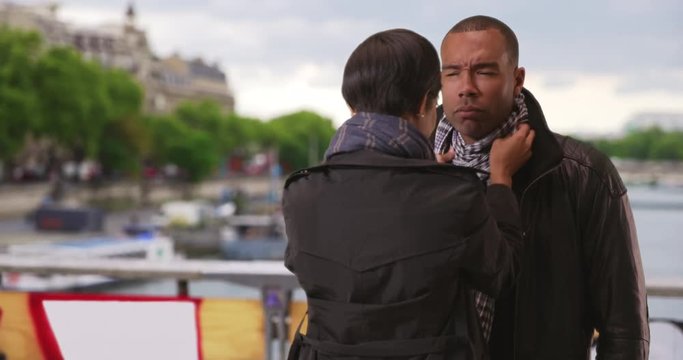 Pretty young African girlfriend fixing up her boyfriend's outfit on a cold day in Paris, France, Handsome ethnic boyfriend gets his scarf rearranged by his girlfriend, 4k